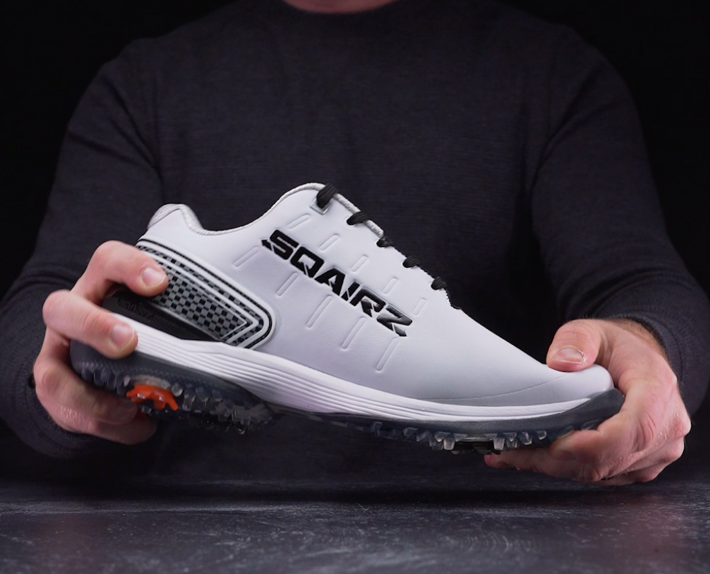 Man tries to twist a white golf shoe between his hands. 